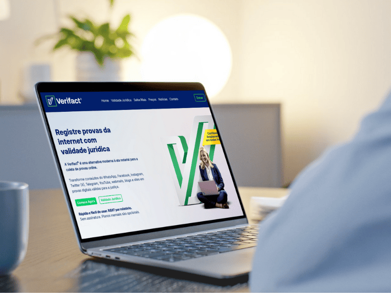 A imagem mostra um homem com o notebook em cima da mesa. Na tela, está aberta a página inicial do site da Verifact.