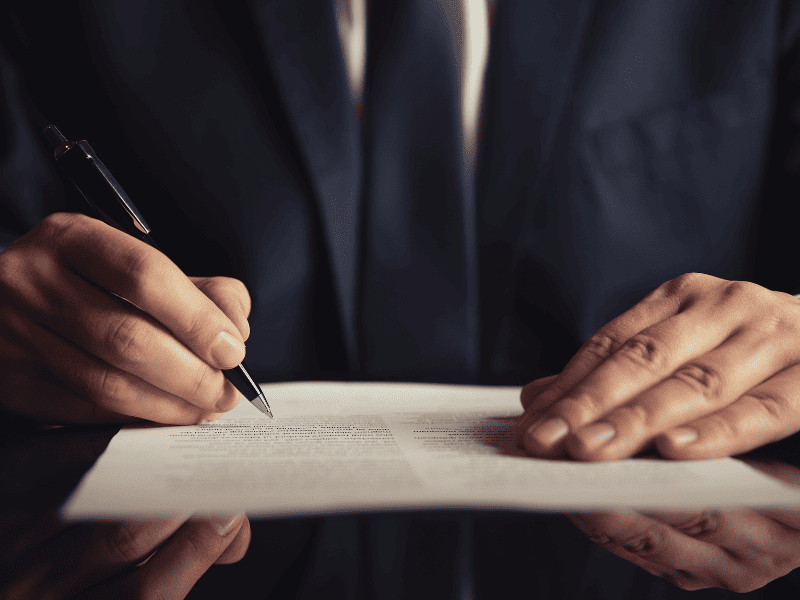 Pessoa de terno assinando um documento colocado sobre a mesa