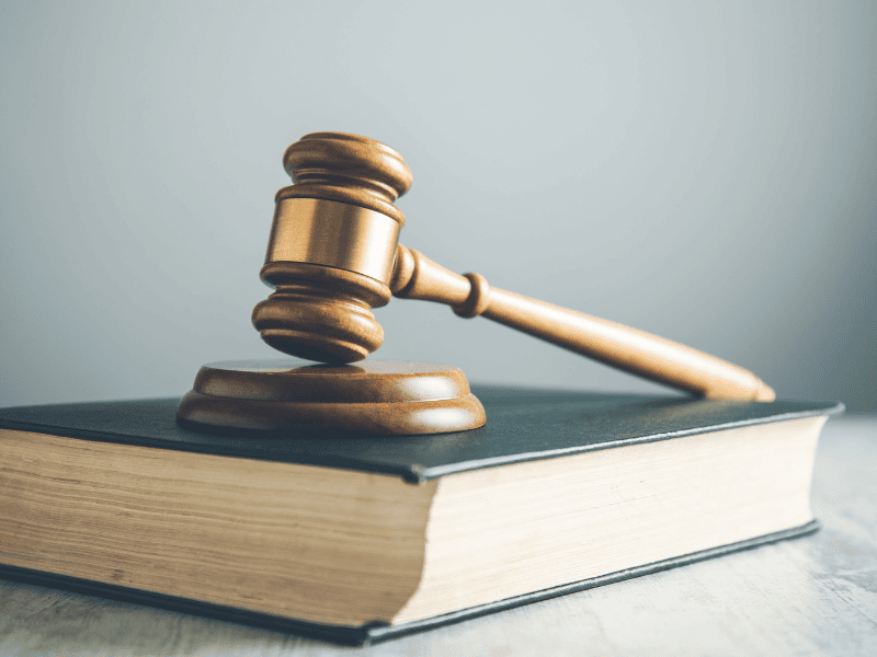 Martelo de juiz apoiado sobre um livro grosso de capa escura.
