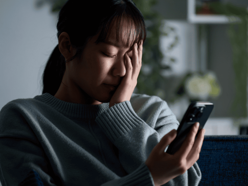 Mulher com a mão no rosto de indignação após ler alguma postagem difamatória no celular 