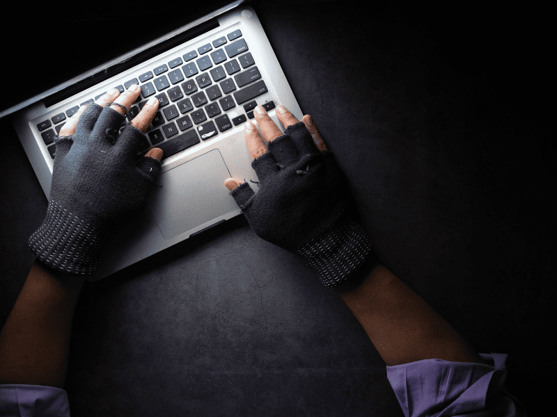 Pessoa usando luvas digitando em um notebook, representando atividade criminosa online.
