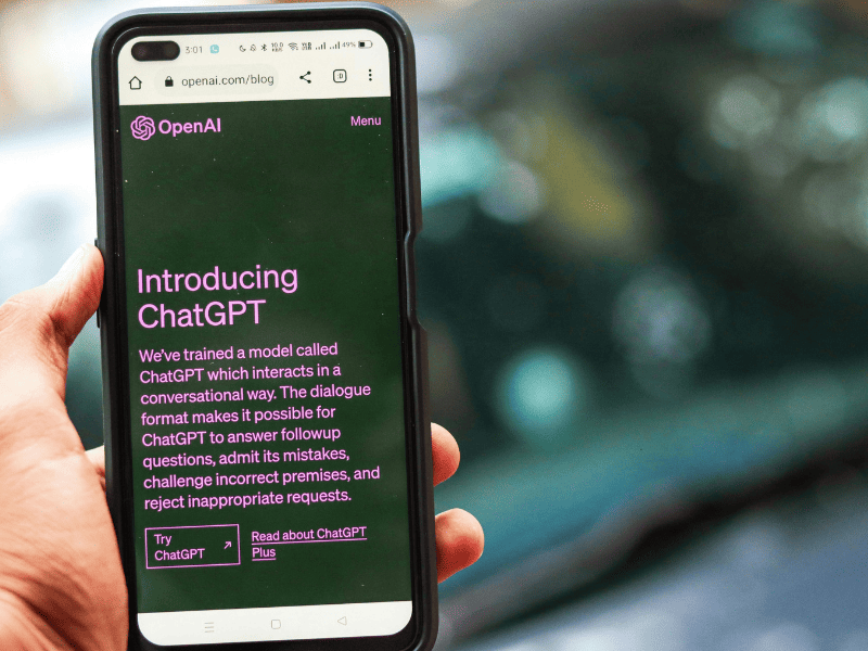 Pessoa segurando smartphone com a página do ChatGPT aberta no site da OpenAI exibida na tela
