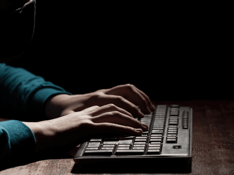 Mãos digitando em um teclado em ambiente escuro, com iluminação focada e fundo preto