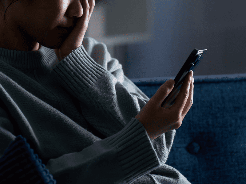 Pessoa olhando para a tela de um celular com expressão de preocupação, representando o impacto emocional de ofensas ou injúria no ambiente digital.
